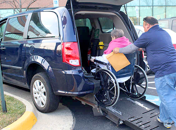 a man maneuvering a wheelchair with an elderly woman into a van