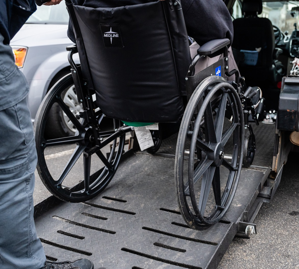 a staff pushing a person in a wheelchair into a van