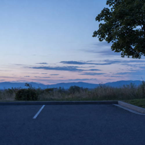 Empty asphalt parking space in bright summer sun with heat shimmer and a small patch of tree shade