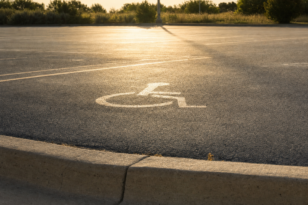 Empty sun-baked asphalt parking lot with heat haze and a faded accessible parking symbol on the ground